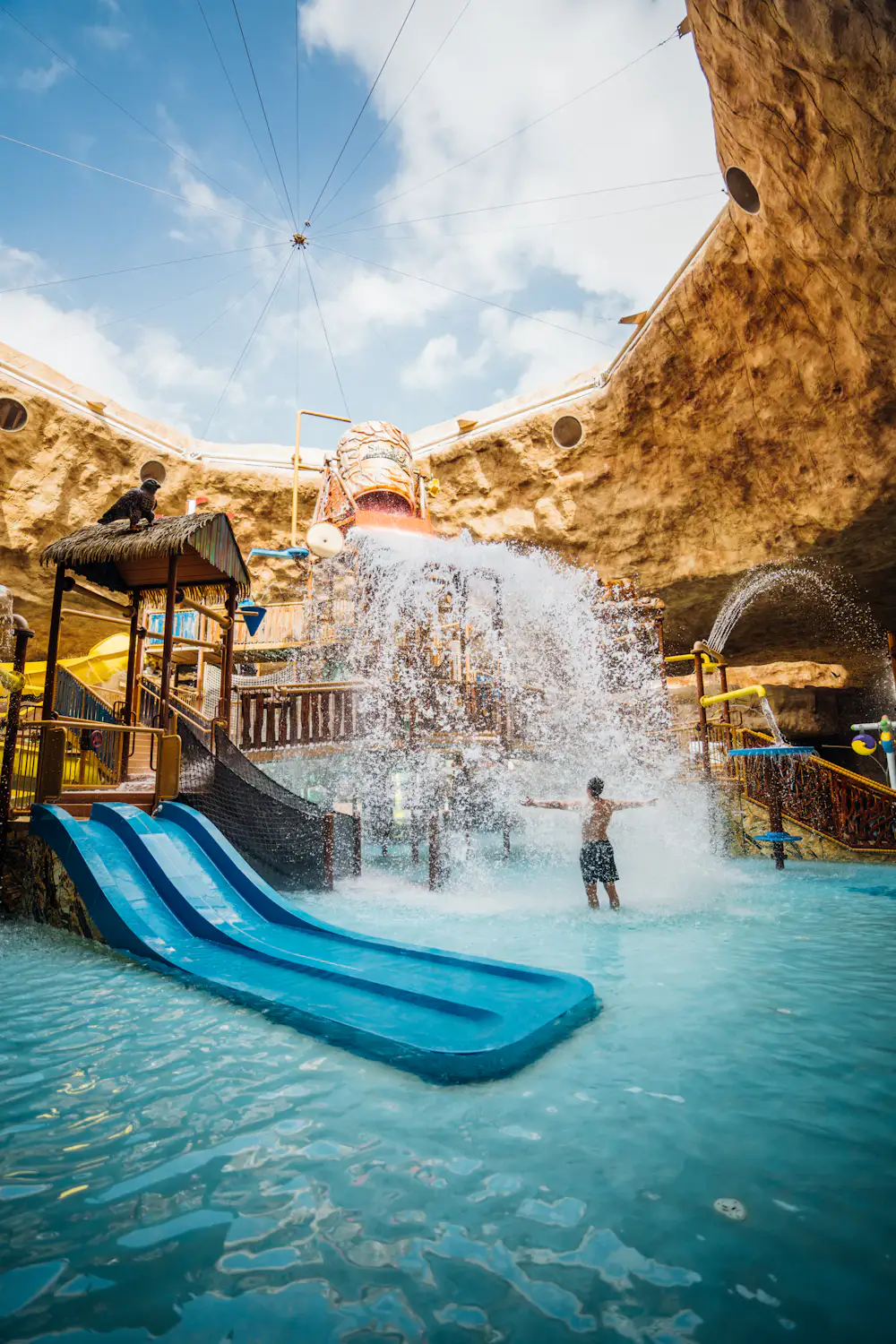 Illustrative family water-play area with blue slides and a splash bucket